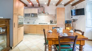 Eine Küche mit Holzschränken, einem Esstisch mit Stühlen und einem an der Wand befestigten Fernseher.