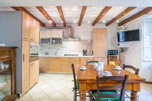 A kitchen with wooden cabinets, a dining table with chairs, and a TV mounted on the wall.