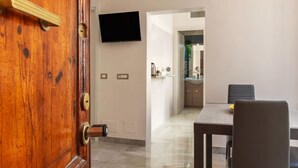 A wooden door with a keyhole, a wall-mounted TV, a dining area with a table and chairs, and a kitchen visible in the background. - GuestHost - Sweety Apartment near MM Ottaviano (Roma)