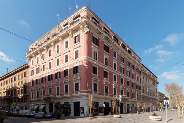 A large, multi-story building with a classical architectural style, featuring a prominent corner entrance and a series of windows.