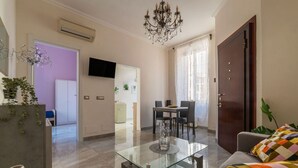 A living room with a glass coffee table, a chandelier, a sofa, and a TV mounted on the wall. - GuestHost - Sweety Apartment near MM Ottaviano (Roma)