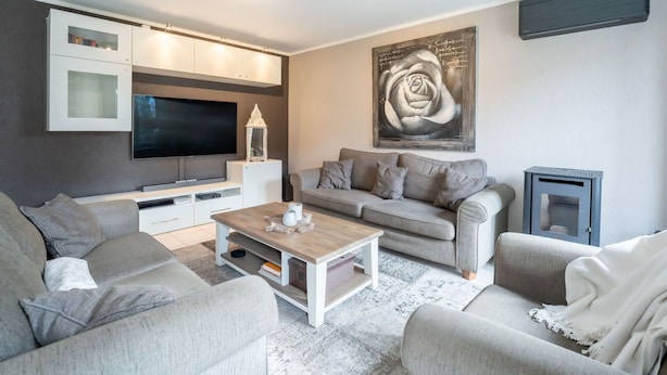 Un salón moderno con un televisor de pantalla plana, un sofá gris, una mesa de centro y un cuadro abstracto grande.