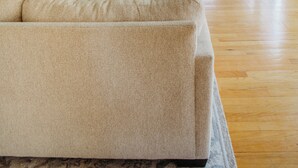 Un salon spacieux avec un grand canapé beige, un téléviseur à écran plat fixé au mur et une plante en pot.