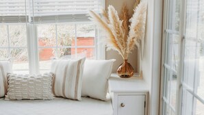 Une pièce chaleureuse avec une banquette intégrée, un petit meuble et une fenêtre avec des stores blancs.