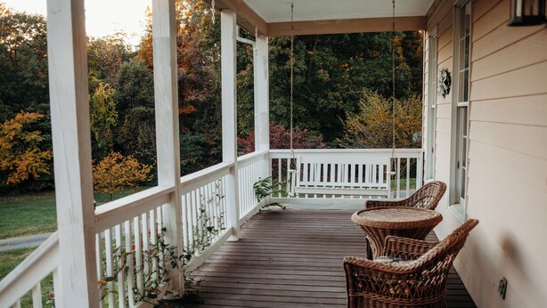 Une véranda en bois avec des balustrades blanches et des chaises en osier.
