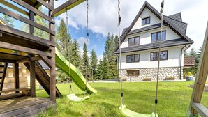 A playground with a slide and swings, a stone house, and a grassy yard. - Beautiful private villa for 20 people with WIFI, TV, patio and panoramic view (Koscielisko)