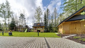 A wooden cabin with a sloped roof, surrounded by a paved walkway and a grassy area with a playground. - Beautiful private villa for 20 people with WIFI, TV, patio and panoramic view (Koscielisko)