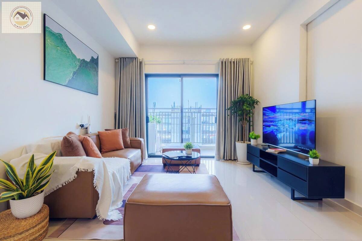 A modern living room with a sofa, ottoman, and a TV on a black stand.