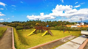 A playground with slides and swings, surrounded by grass and trees, under a clear sky. - Posada Doña Lucilia.  Comfort, elegance and beauty.  Your home away from home. (Mixco)