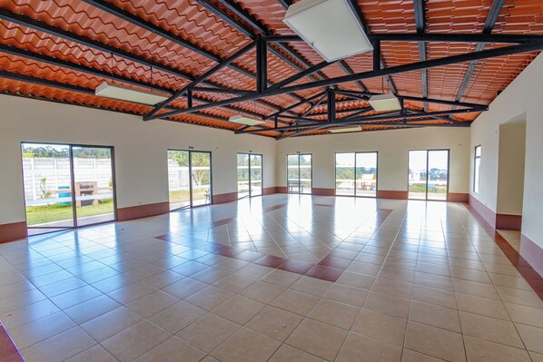 A spacious indoor area with large windows, a tiled floor, and a corrugated metal roof.