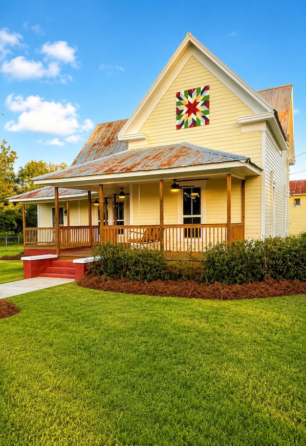 A two-story building with a porch, a large quilt on the wall, and a well-maintained lawn.