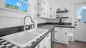 A kitchen with white cabinets, black and white checkered backsplash, and a window with a view of greenery. - Pet Friendly • Fenced Yard • Near Statesboro (Metter)