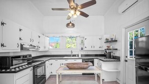 A kitchen with white cabinets, a black refrigerator, a wooden bowl on a table, and a ceiling fan. - Pet Friendly • Fenced Yard • Near Statesboro (Metter)