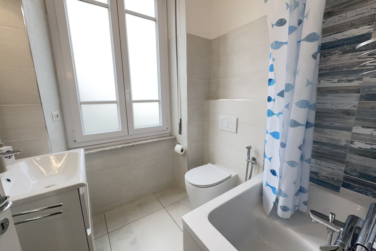 A bathroom with a toilet, sink, bathtub, and a window.