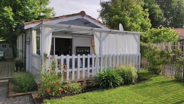 A covered outdoor seating area with a white fence, surrounded by a well-maintained garden with various plants and flowers. - Chalet grand confort Bassin d'Arcachon - Chalet les solariales (La Teste De Buch)
