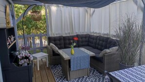 A covered patio with a cushioned seating area, a small table with a vase, and a patterned rug. - Chalet grand confort Bassin d'Arcachon - Chalet les solariales (La Teste De Buch)