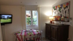 A dining area with a table set for two, a television mounted on the wall, and a cabinet with a lamp. - Chalet grand confort Bassin d'Arcachon - Chalet les solariales (La Teste De Buch)
