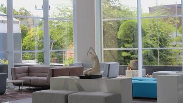 A modern living room with a sectional sofa, a coffee table, and a blue accent chair. There is a large window providing a view of greenery outside.