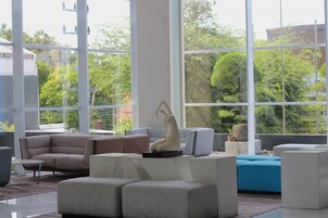 A modern living room with a sectional sofa, a coffee table, and a blue accent chair. There is a large window providing a view of greenery outside.