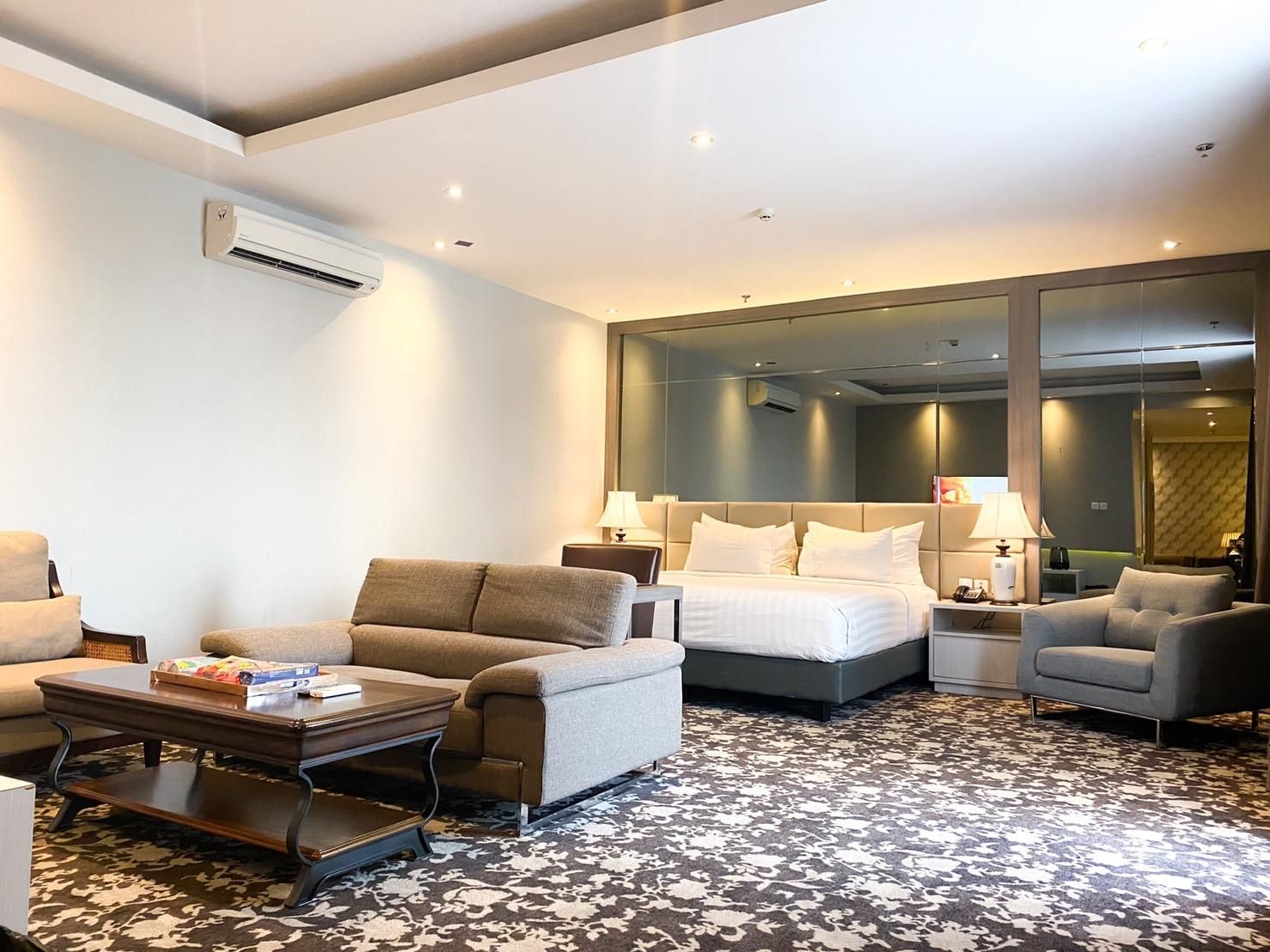 A hotel room with a bed, two armchairs, a sofa, a coffee table, and a large mirror.