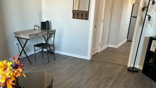 Ein modernes Wohnzimmer mit einem schwarzen Sofa, einem Couchtisch mit Blumen, einem gemusterten Teppich und einem Essbereich mit Holztisch und Stühlen.