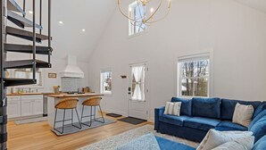 A spacious living area with a blue sofa, a kitchen with white cabinets, and a staircase.