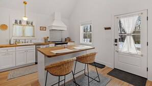 A modern kitchen with white cabinetry, a central island, and a dining area with two bar stools.