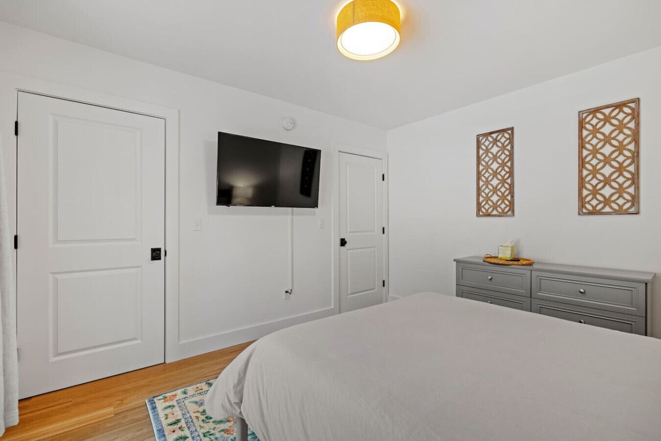 A bedroom with a bed, a TV mounted on the wall, a dresser, and two decorative panels.