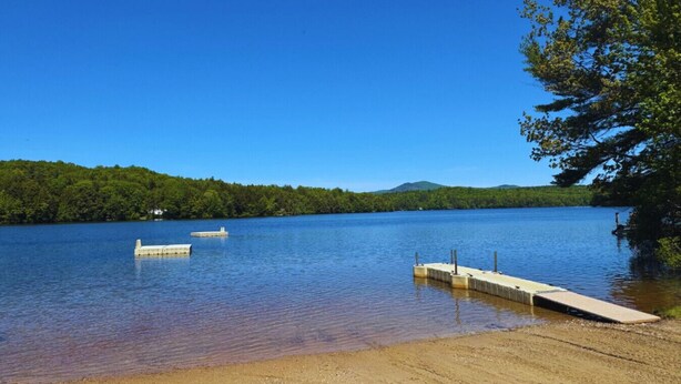 A lake with a sandy beach and a concrete dock extending into the water.