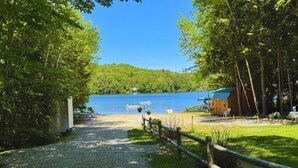 A gravel path leading to a dock over a lake, surrounded by trees and a wooden cabin.