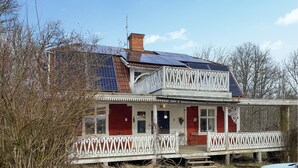 Une maison à deux étages, avec une façade rouge, des balustrades de balcon blanches et des panneaux solaires sur le toit.