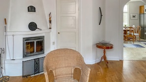 Un salon avec une cheminée, un fauteuil en osier et une table ronde sur laquelle se trouve un panier en fil de fer.