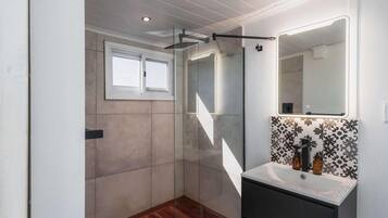Een moderne badkamer met douche, wastafel en spiegel, en een raam.