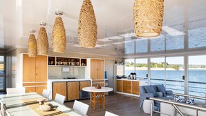 A modern kitchen with wooden cabinets, a bar area, and large windows overlooking a body of water. - Chobe Princesses By Mantis (Kasika)