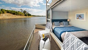 A room with a bed, a table with a glass of beer, and a camera on a stool. - Chobe Princesses By Mantis (Kasika)