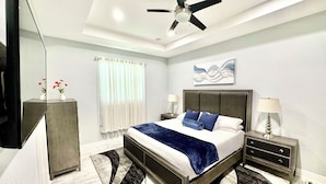 A modern bedroom with a bed, nightstands, a ceiling fan, a large mirror, and a window with curtains.