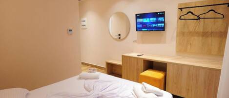 Habitació d'hotel amb llit, tocador de fusta amb mirall, televisió de pantalla plana i una banca de fusta.