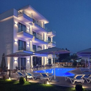 A modern multi-story hotel with a swimming pool, outdoor seating, and umbrellas. - Hotel Alexander (Sarandë)