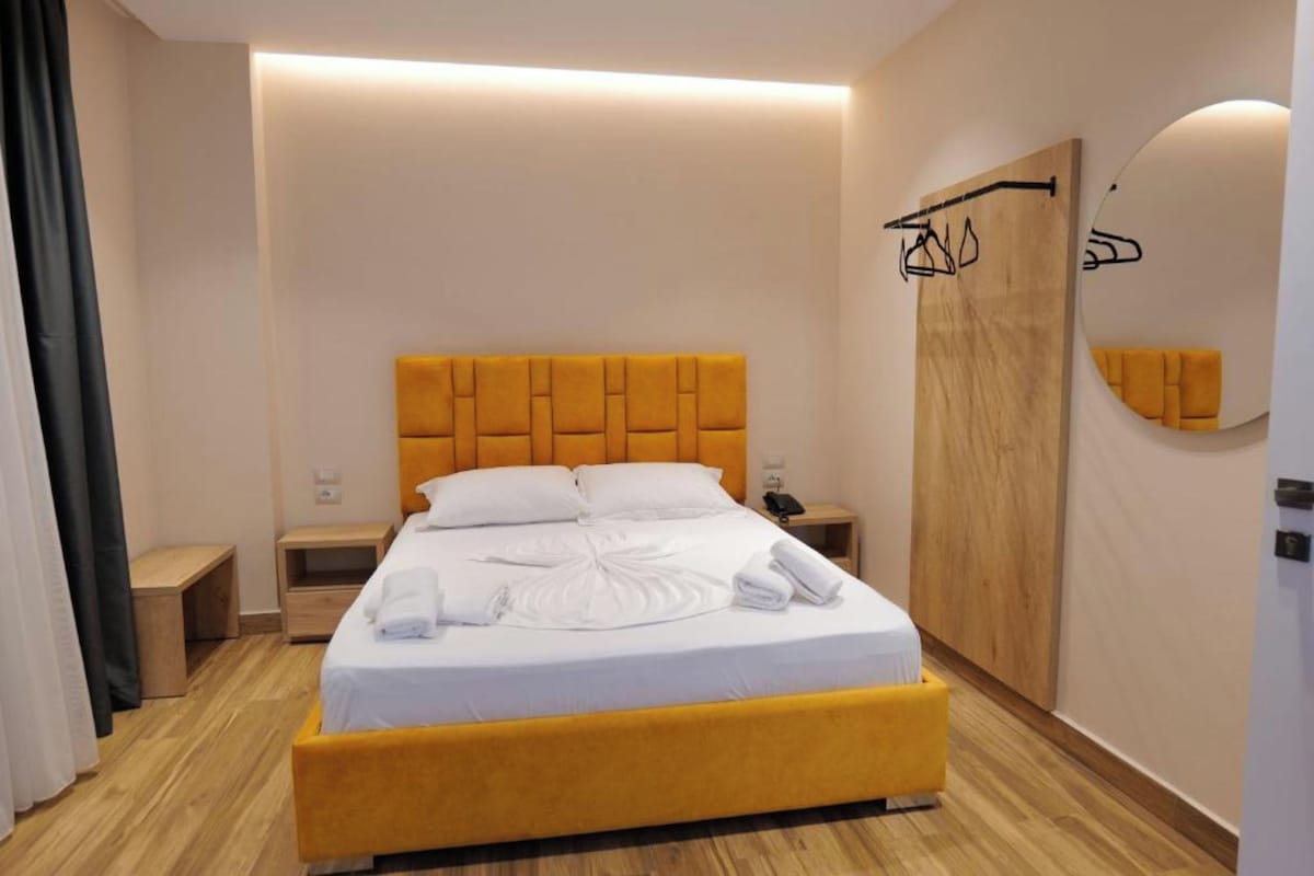 A hotel room with a bed, bedside tables, a wardrobe, and a mirror.
