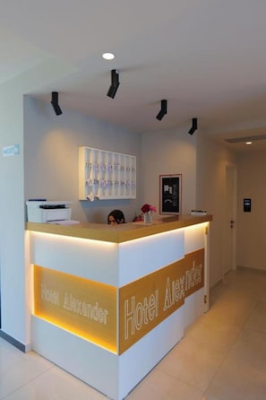 A hotel reception desk with a modern design, a nameplate, and a framed picture on the wall. - Hotel Alexander (Sarandë)