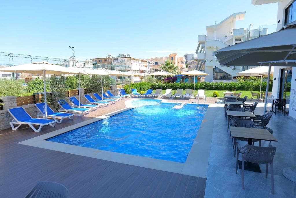A swimming pool with sun loungers and umbrellas, surrounded by outdoor seating and a view of residential buildings.