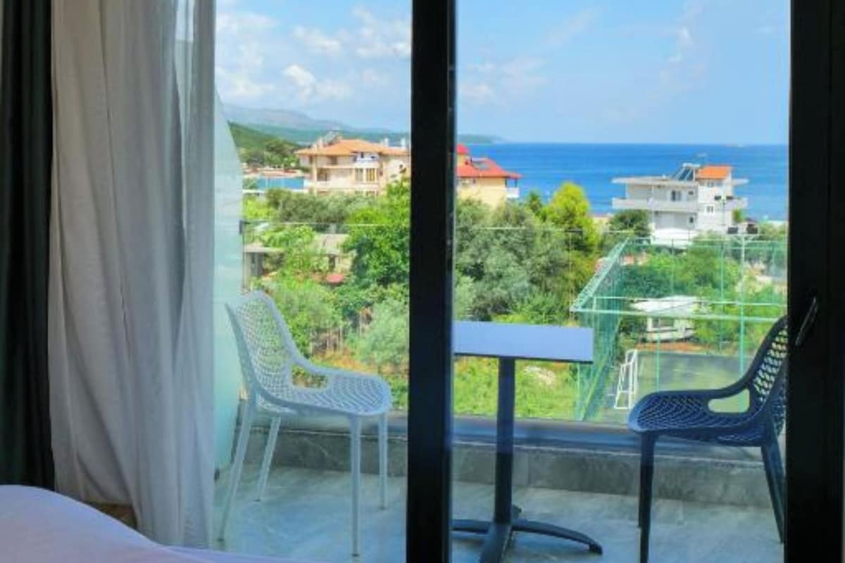 A hotel room with a large window offering a view of the sea and surrounding buildings.