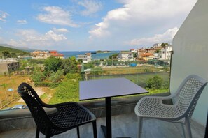 Varanda com mesa e duas cadeiras, vista para área costeira com casas e quadra de tênis.