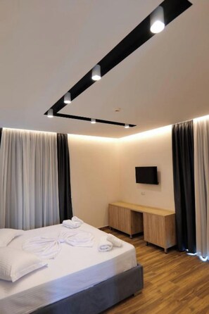Quarto de hotel moderno com cama, mesa de cabeceira e televisão de tela plana fixada na parede.
