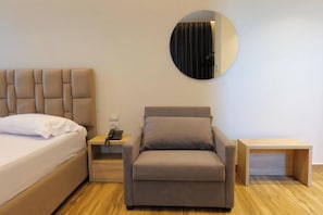 A modern hotel room with a bed, a sofa, a bedside table with a phone, and a small wooden nightstand. - Hotel Alexander (Sarandë)