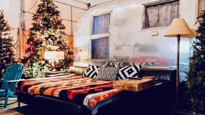 Une chambre confortable avec un lit, un sapin de Noël et, au fond, un camping-car.