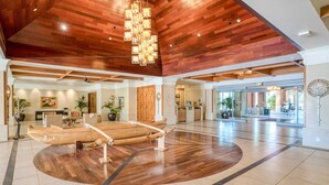 A spacious lobby with a wooden ceiling, a reception desk, and a seating area with a circular wooden table. - Maui Resort Rentals: Honua Kai - 5 Total Bedrooms, Ground Floor Interior Courtyard, Steps to Pools, Beach, BBQs! (Lahaina)