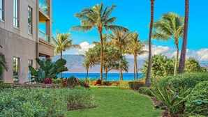 A hotel courtyard with a well-maintained lawn, palm trees, and a view of the ocean. - Maui Resort Rentals: Honua Kai - 5 Total Bedrooms, Ground Floor Interior Courtyard, Steps to Pools, Beach, BBQs! (Lahaina)