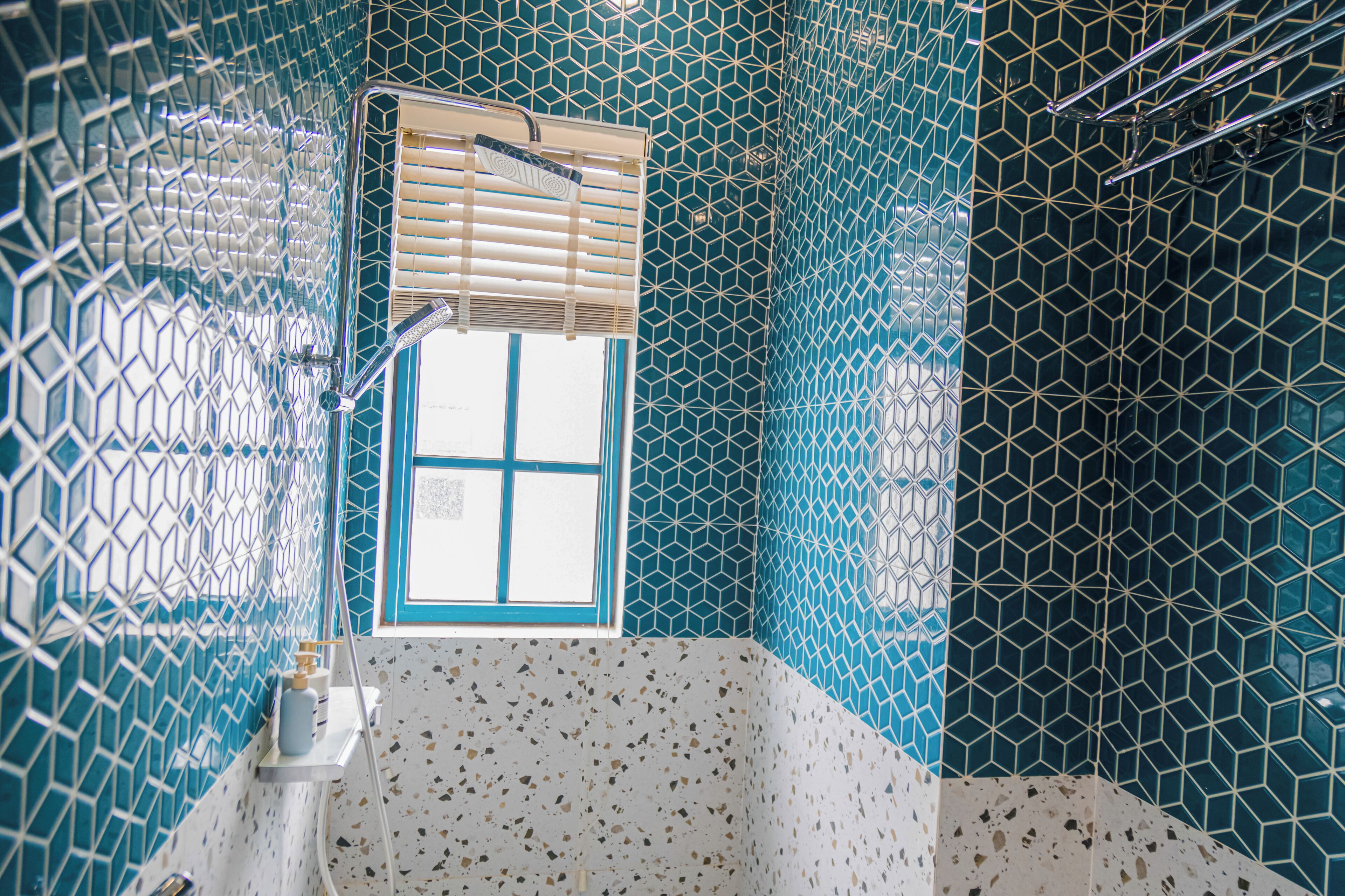 A bathroom with a geometric tile pattern, a window with blinds, and a shower area.