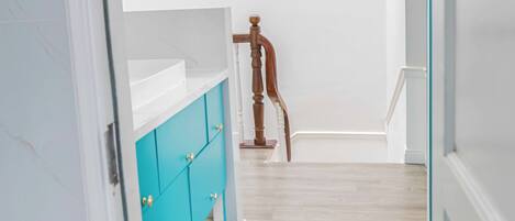 A narrow hallway with a wooden door, a blue mat, and a white cabinet with teal doors.